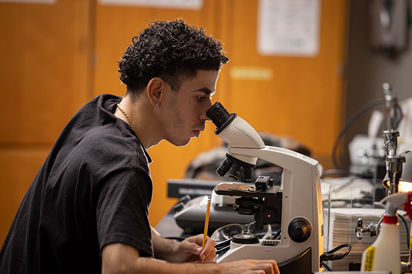 Male student in lab using microscope